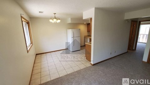 A spacious living room with a carpeted floor and a white refrigerator in the corner.