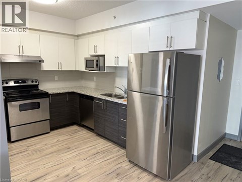 A modern kitchen with a stainless steel refrigerator and wooden flooring.
