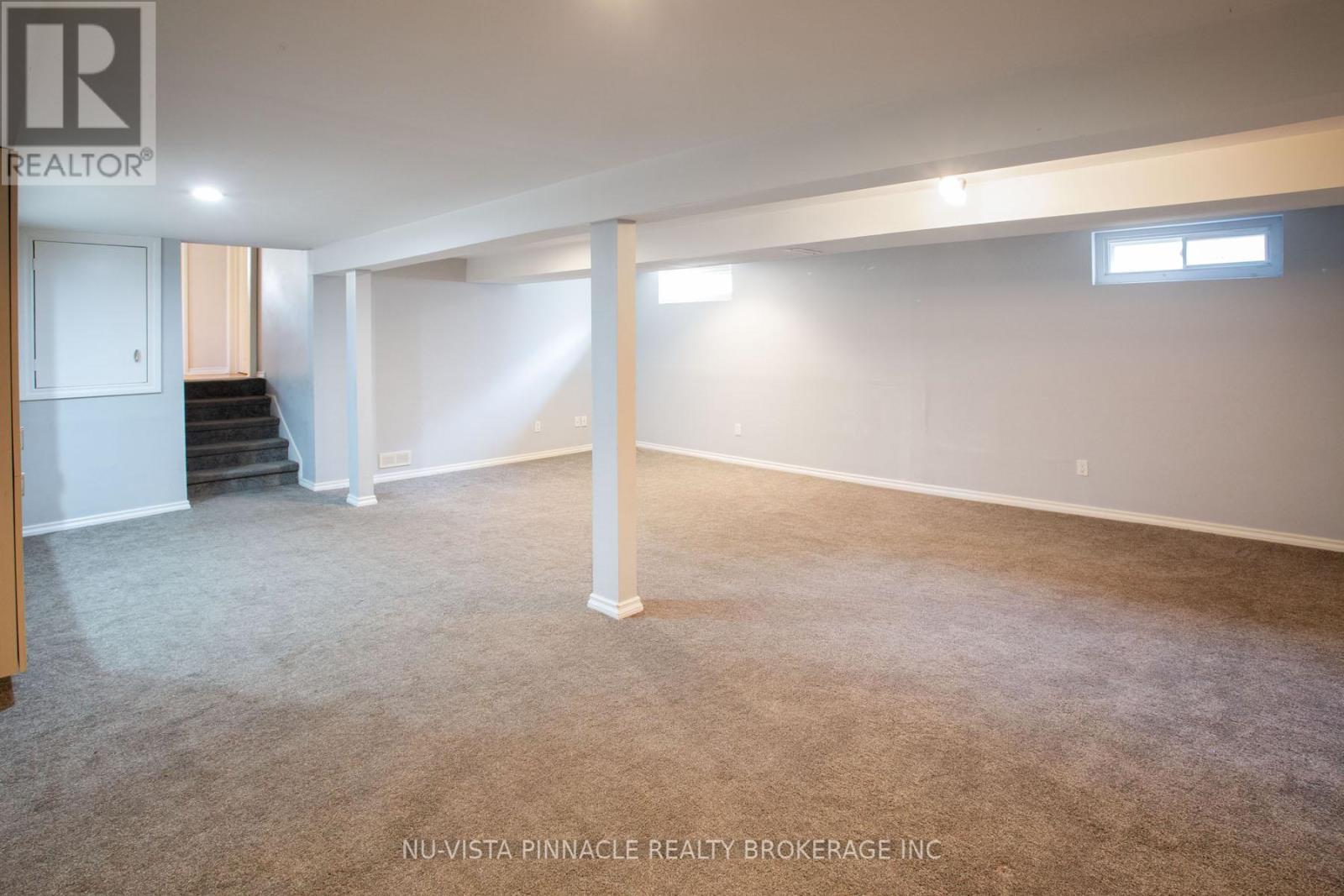 A spacious room with a carpeted floor and a staircase leading to another level.