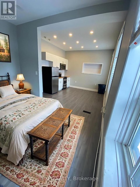 A bedroom with a bed, a rug, and a refrigerator in the kitchen area.