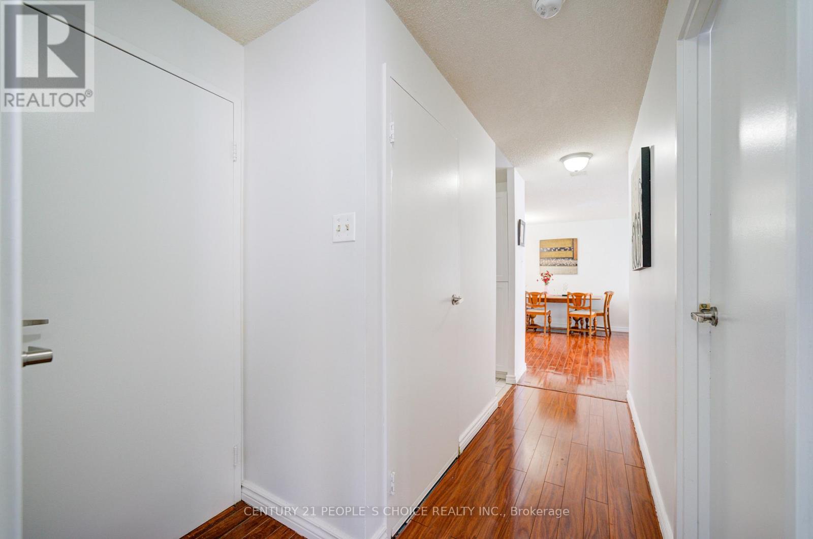 A hallway with white walls and wood flooring leading to a dining area.