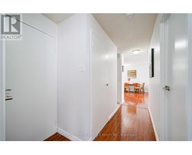 A hallway with white walls and wood flooring leading to a dining area.