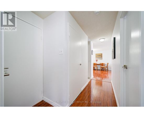 A hallway with white walls and wood flooring leading to a dining area.