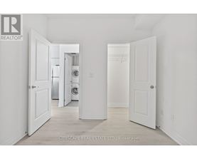 A real estate listing photo of a white bedroom with a washer and dryer in the background.