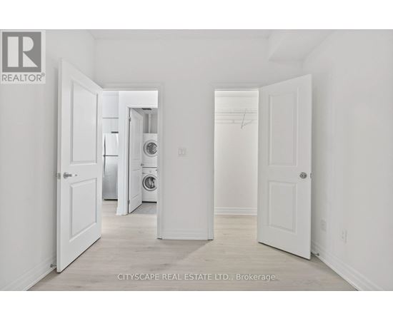 A real estate listing photo of a white bedroom with a washer and dryer in the background.