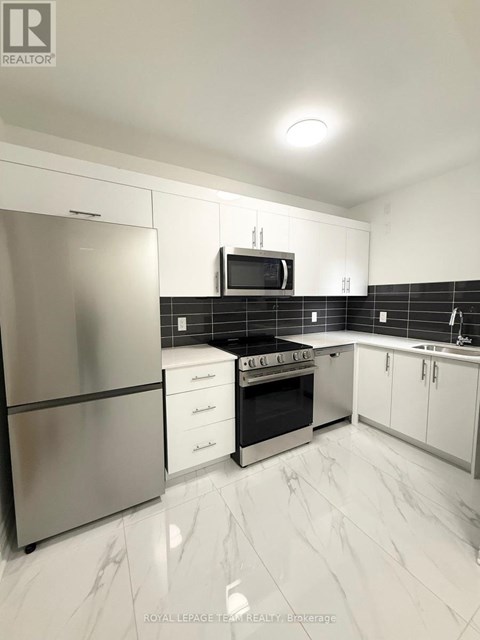 A modern kitchen with a stainless steel refrigerator, microwave, oven, and white cabinets.