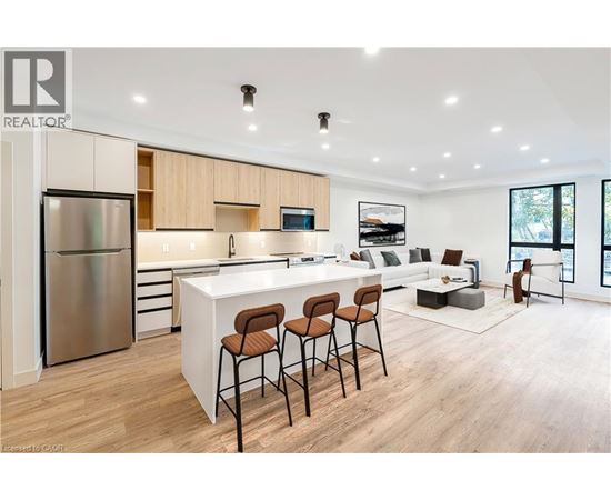 A modern kitchen with a refrigerator, bar stools, and a dining table.