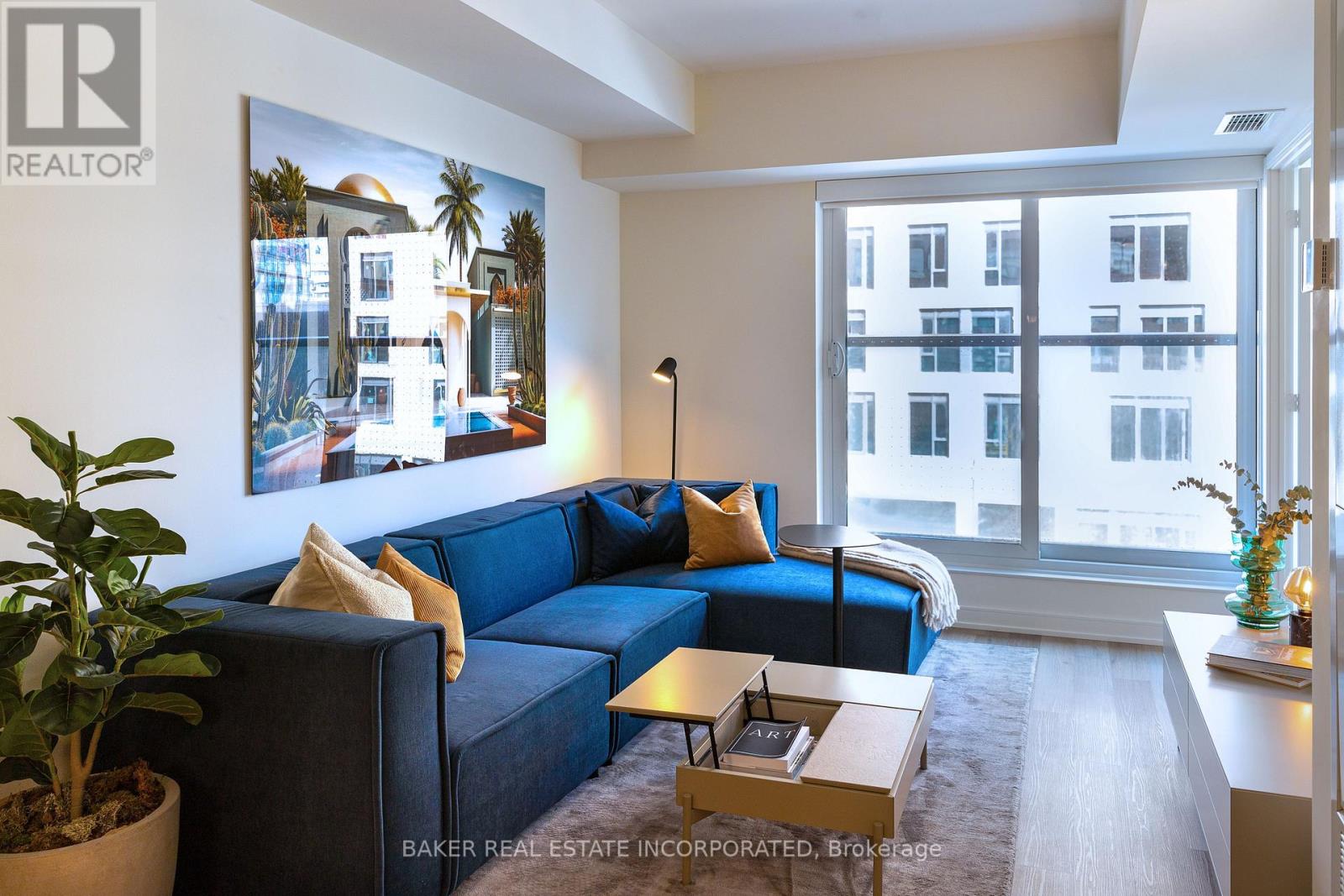 A living room with a blue couch and a painting of a building on the wall.