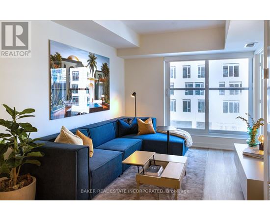 A living room with a blue couch and a painting of a building on the wall.