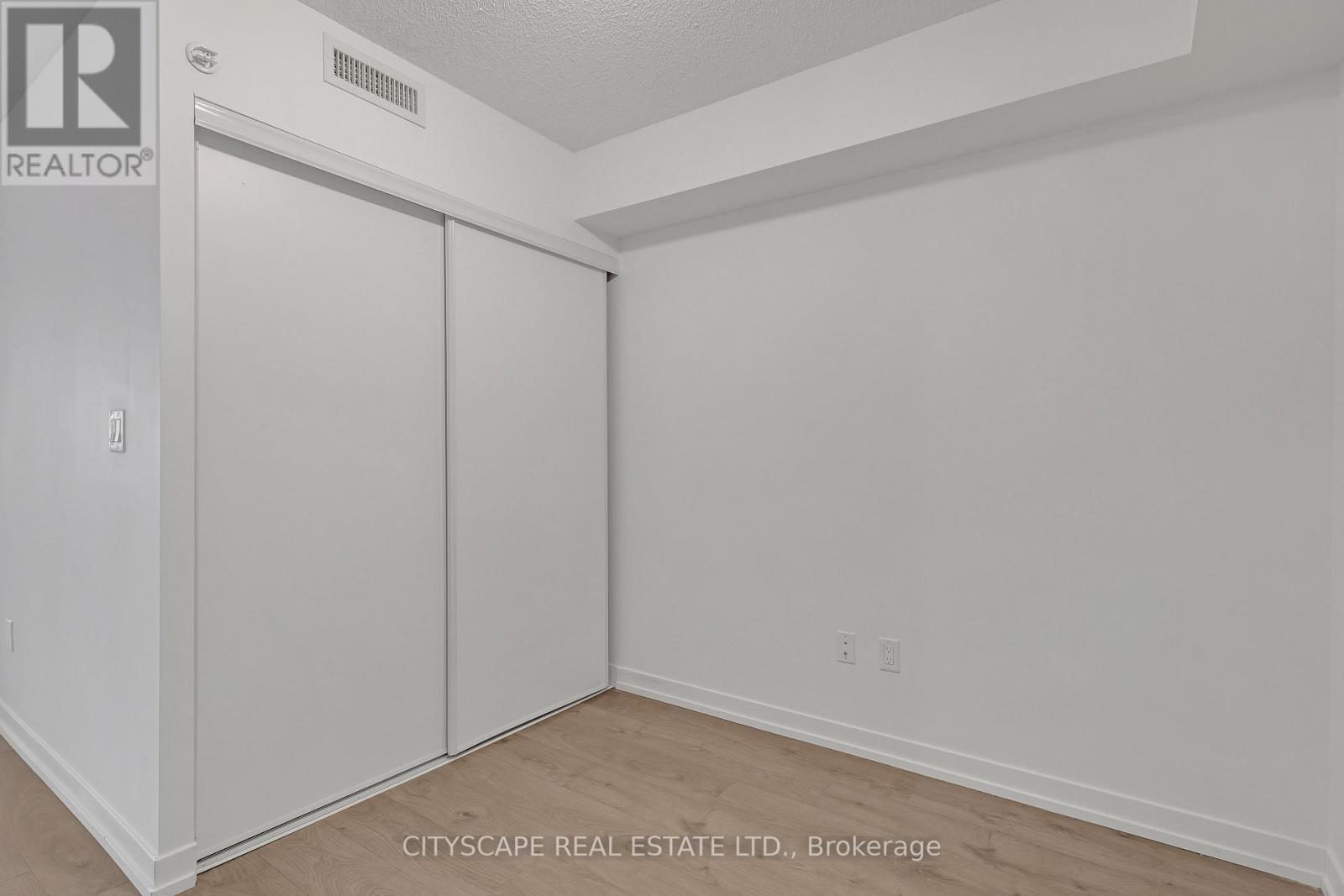 A white bedroom with a sliding door closet and a realtor sign on the wall.