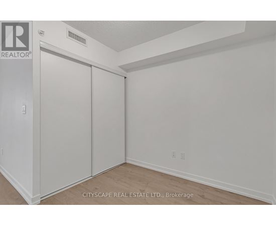 A white bedroom with a sliding door closet and a realtor sign on the wall.