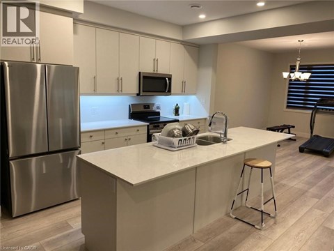A kitchen with a refrigerator, microwave, and a counter with a stool.
