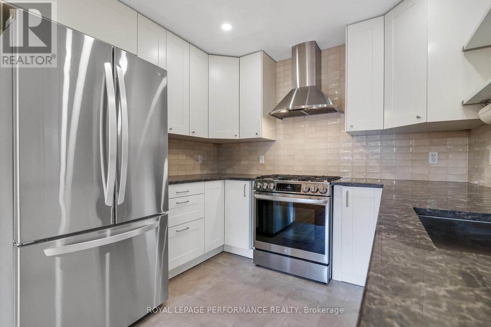 A modern kitchen with a stainless steel refrigerator and a stainless steel range hood.