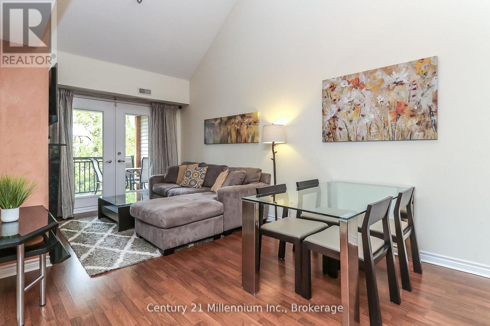 A living room with a glass table and chairs, a grey couch, and a painting on the wall.