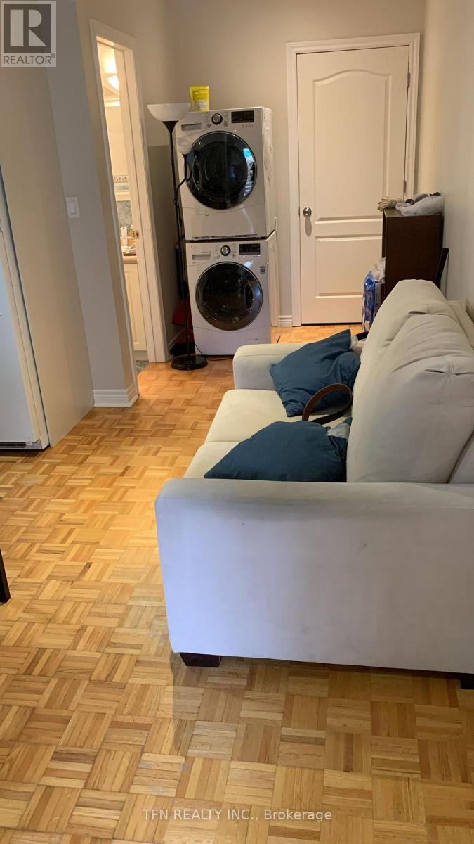 A white couch with a blue pillow sits in a room with a washing machine in the background.
