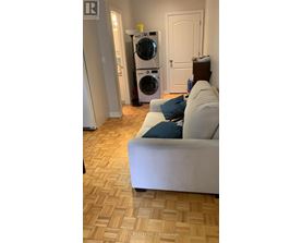 A white couch with a blue pillow sits in a room with a washing machine in the background.