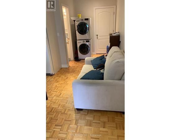 A white couch with a blue pillow sits in a room with a washing machine in the background.