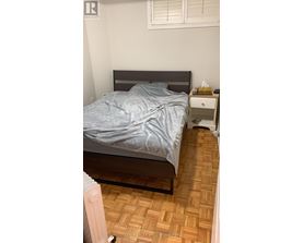 A bedroom with a bed, nightstand, and a wooden floor.