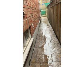 A wet brick walkway leads from a white door.