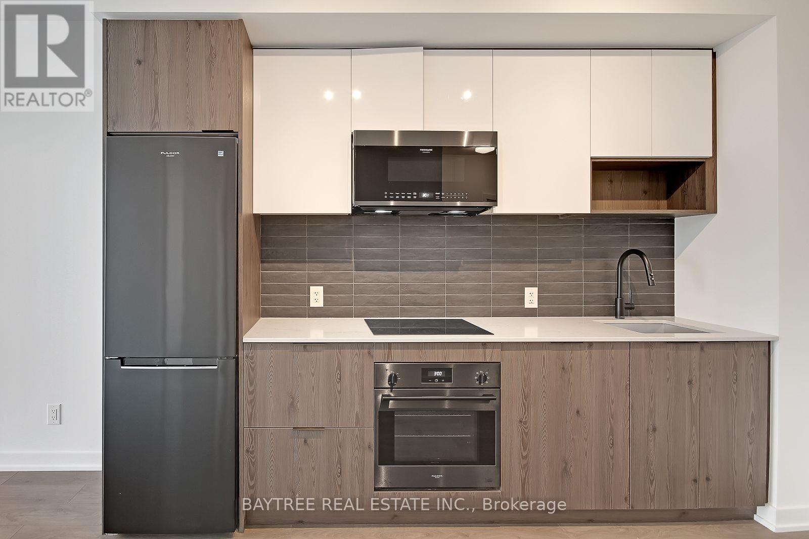 A modern kitchen with a refrigerator, microwave, oven, and sink.