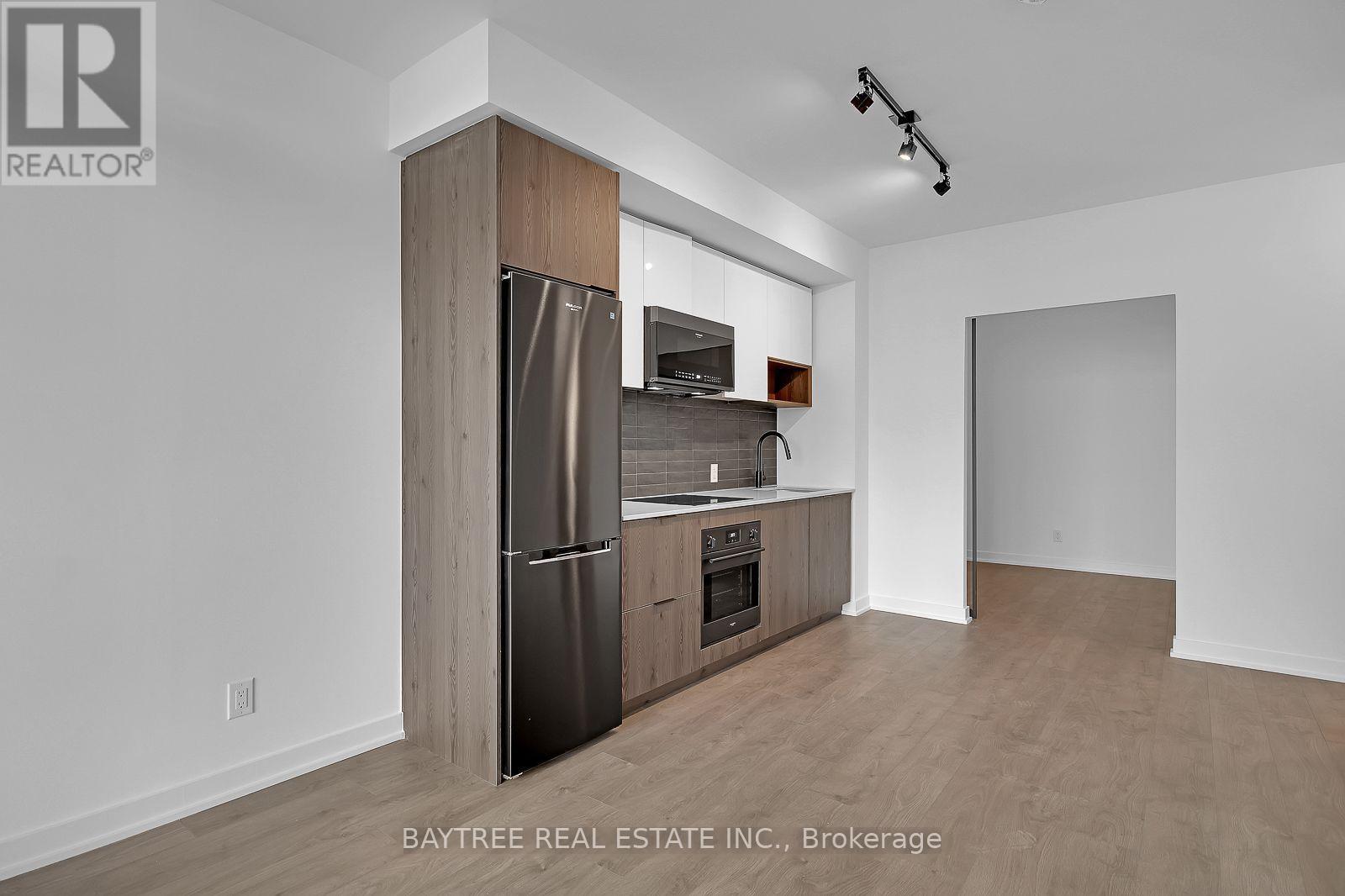 A kitchen with a refrigerator, oven, and microwave in a white room.