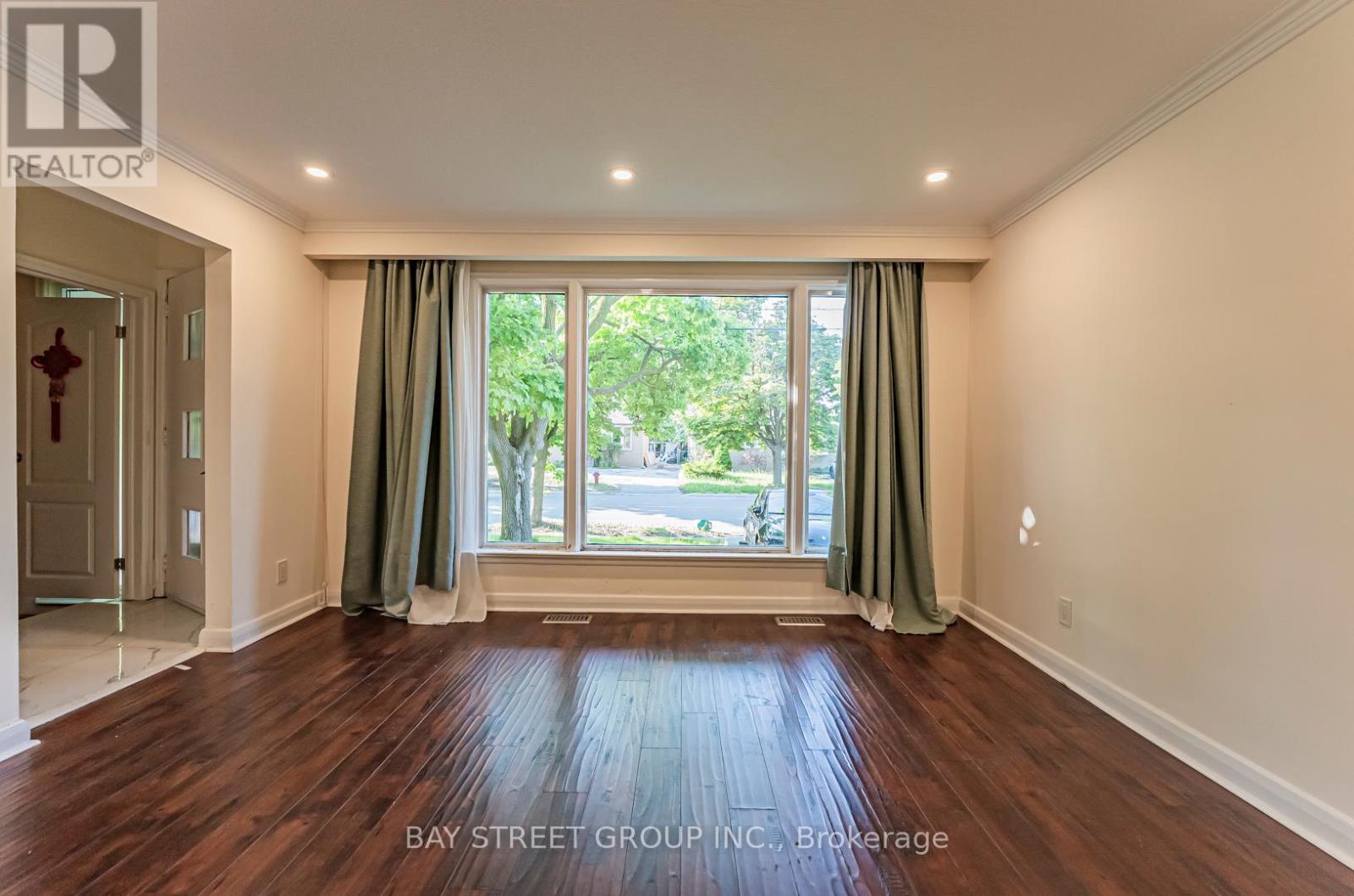A room with wooden flooring and a large window with green curtains.