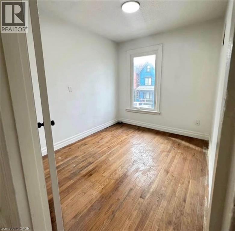 A room with wooden flooring and a window showing a blue house outside.