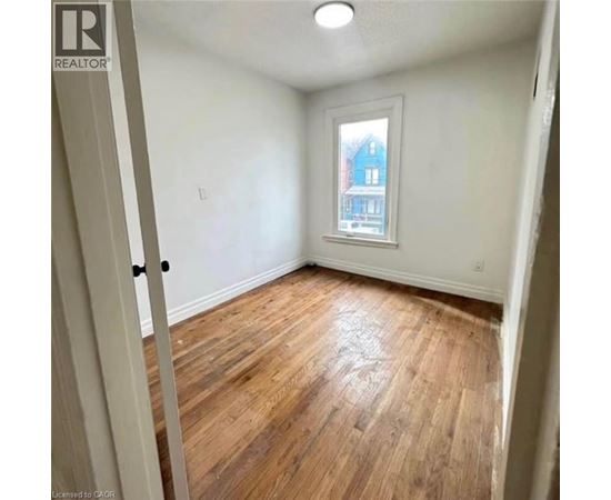 A room with wooden flooring and a window showing a blue house outside.