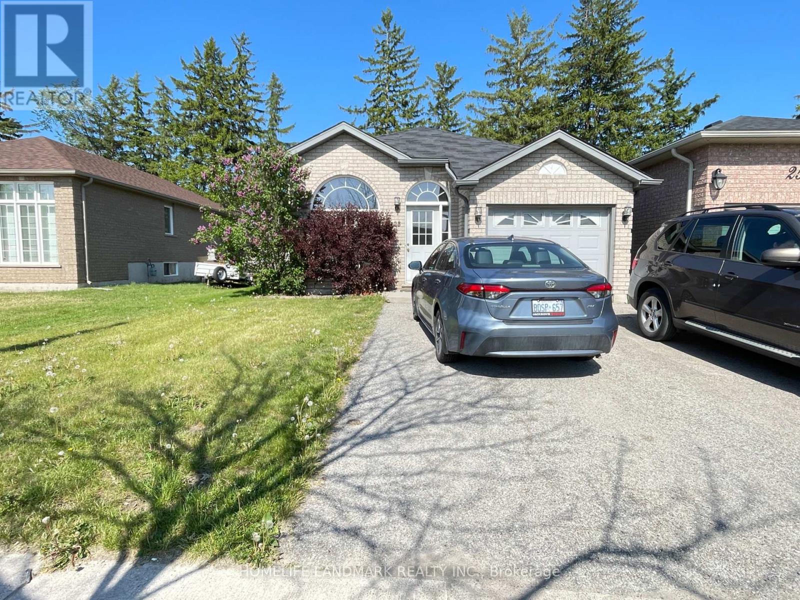 A grey car is parked in front of a house with a tree in the front yard.