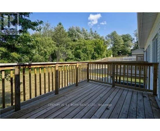 A wooden deck with a railing and a view of trees and a house.