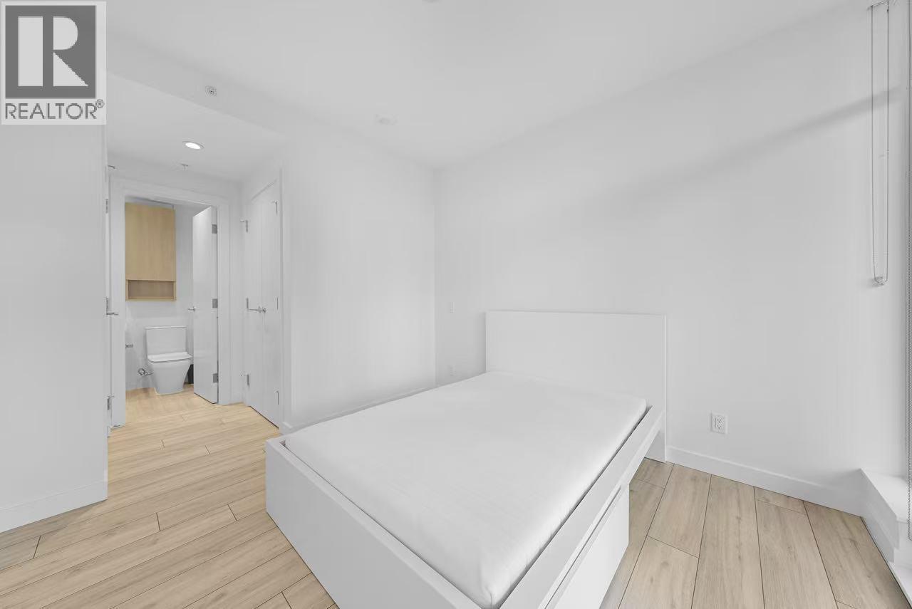 A bedroom with a bed, wooden floors, and a white wall.