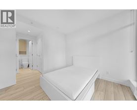 A bedroom with a bed, wooden floors, and a white wall.
