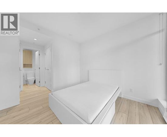 A bedroom with a bed, wooden floors, and a white wall.