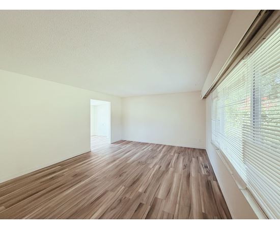 A room with wooden flooring and a window with blinds.