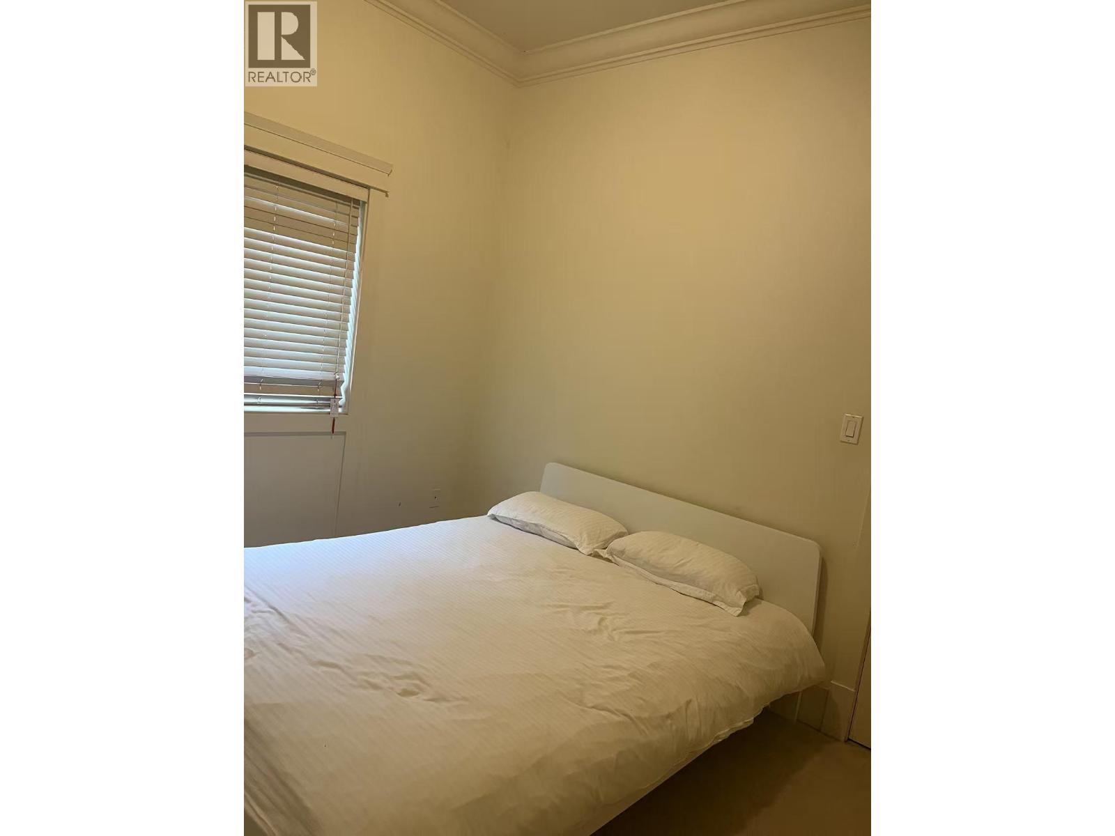 A bedroom with a bed, pillows, and a window with blinds.