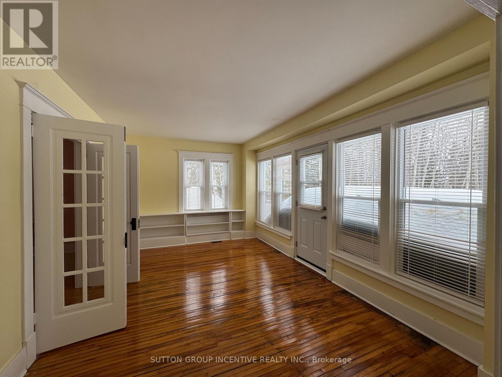 A room with wooden floors and white walls, with a window showing a view of a parking lot.