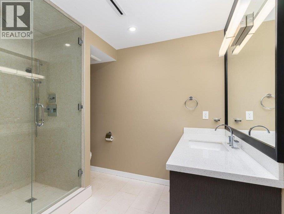 A bathroom with a glass shower stall and a sink with a mirror above it.