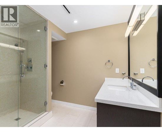 A bathroom with a glass shower stall and a sink with a mirror above it.
