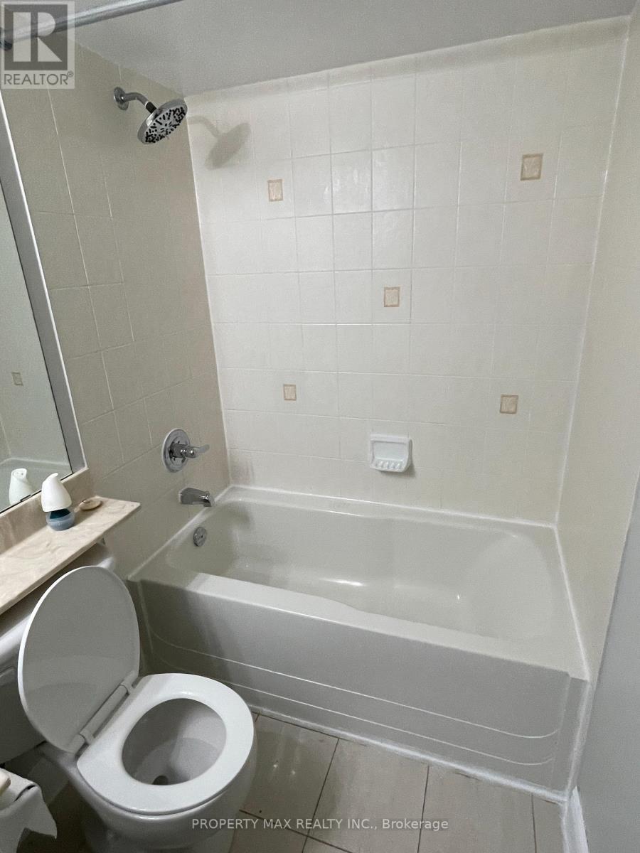 A white toilet is in a bathroom with a white tub.