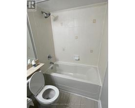 A white toilet is in a bathroom with a white tub.