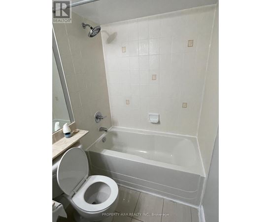 A white toilet is in a bathroom with a white tub.