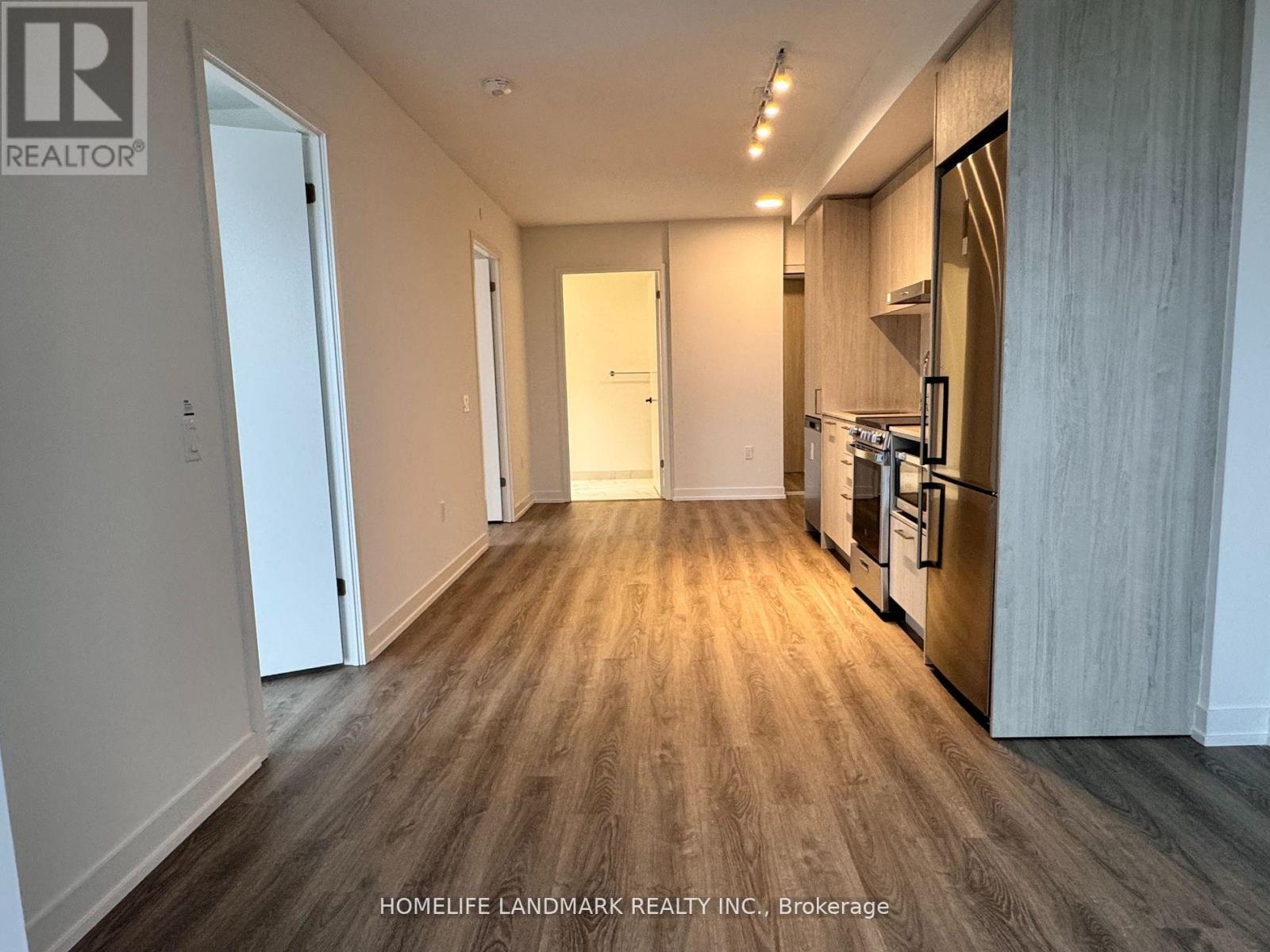 A spacious kitchen with wooden flooring and a refrigerator on the right side.