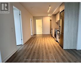 A spacious kitchen with wooden flooring and a refrigerator on the right side.