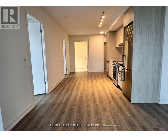 A spacious kitchen with wooden flooring and a refrigerator on the right side.