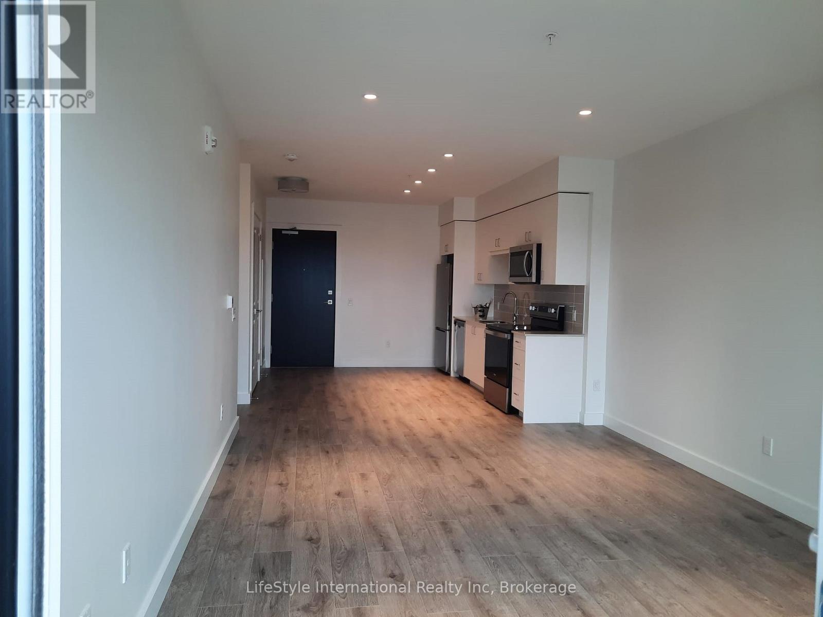 A spacious room with wooden flooring and a kitchen area in the background.