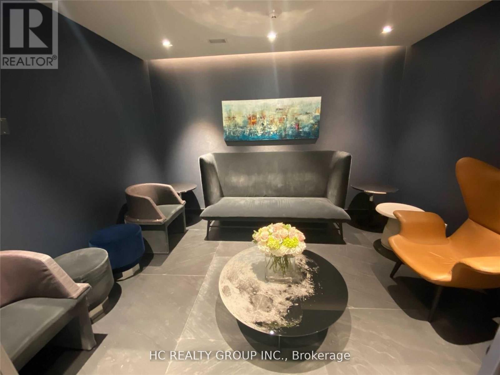 A modern living room with a grey sofa, a coffee table with flowers, and a painting on the wall.