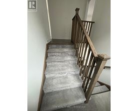A staircase with a wooden railing and grey carpeted steps.