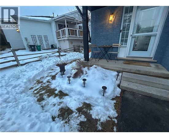A snow-covered ground with a few plants and a wooden fence.