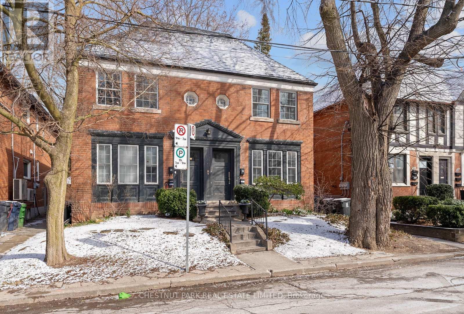 A red brick building with a black door and windows, surrounded by trees and snow.