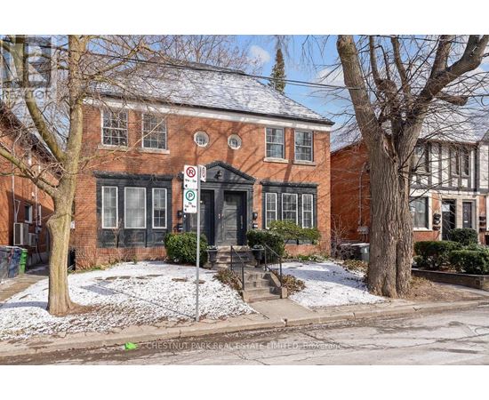 A red brick building with a black door and windows, surrounded by trees and snow.